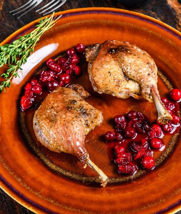 Muslos de pato en salsa de arándanos presentados en plato marrón con tomillo vista de lado