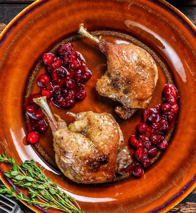 Muslos de pato en salsa de arándanos presentados en plato marrón con tomillo vista desde arriba