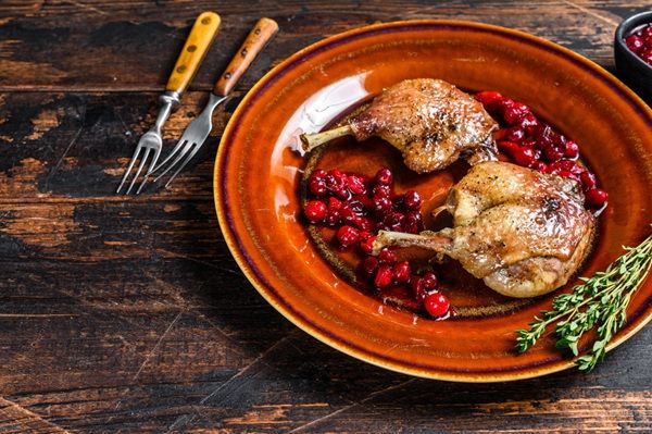 Muslos de pato en salsa de arándanos presentados en plato marrón con tomillo