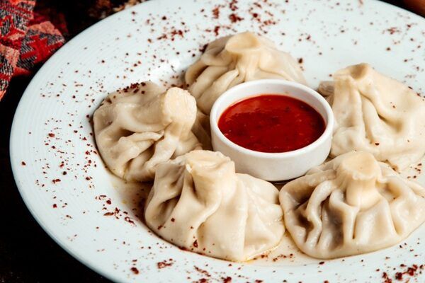 Khinkali presentado en plato blanco con adjika en cuenco pequeño en el centro del plato
