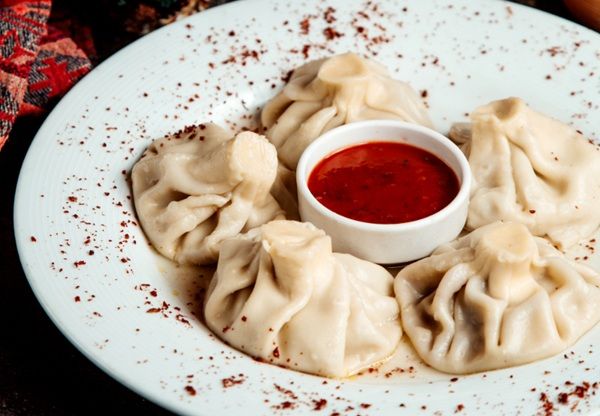 Khinkali presentado en plato blanco con adjika en cuenco pequeño en el centro del plato