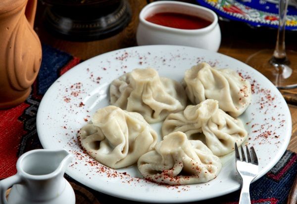 Khinkali presentado en plato blanco con adjika en cuenco pequeño blanco al lado