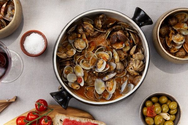 Almejas en salsa de tomate casera de la abuela dentro de olla junto a ingredientes al lado