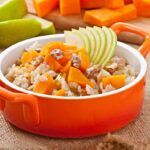 Avena con calabaza, manzanas, nueces y miel presentada en cacerola roja con ingredientes de fondo