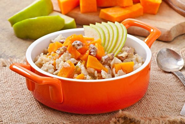 Avena con calabaza, manzanas, nueces y miel presentada en cacerola roja con ingredientes de fondo