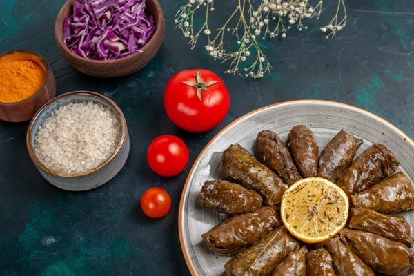 Dolmas presentados en plato blanco con limón en el centro e ingredientes al lado