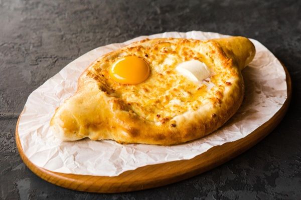 Khachapuri Adjaruli presentada sobre papel y tabla de madera