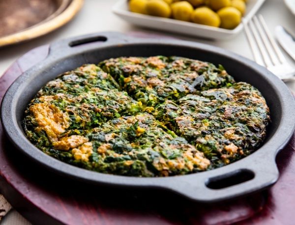 Tortilla persa de hierbas o kuku sabzi presentada en sartén negra sobre tabla de madera