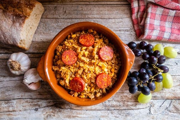 Migas manchegas con chorizo y un racimo de uvas al lado presentadas en cuenco de cerámica