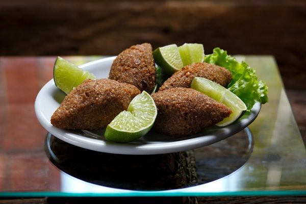 Quibe brasileño presentado en plato blanco junto a limón