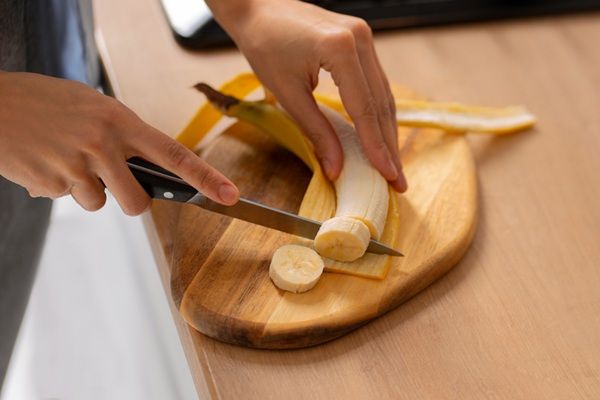 Chef pelando un plátano y cortándolo a rodajas sobre tabla de madera