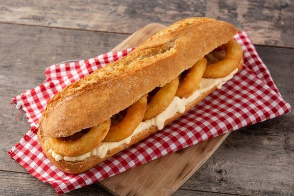Bocadillo de calamares con mayonesa sobre paño a cuadros rojo y tabla de madera
