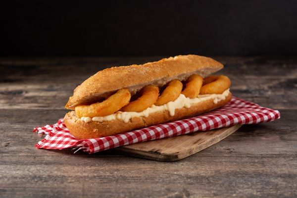 Bocadillo de calamares con mayonesa sobre paño a cuadros rojo y tabla de madera, vista de frente