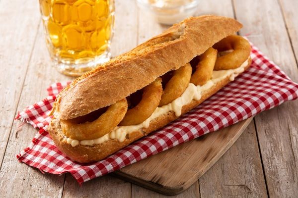Bocadillo de calamares con mayonesa sobre paño a cuadros rojo, tabla de madera y cerveza al fondo